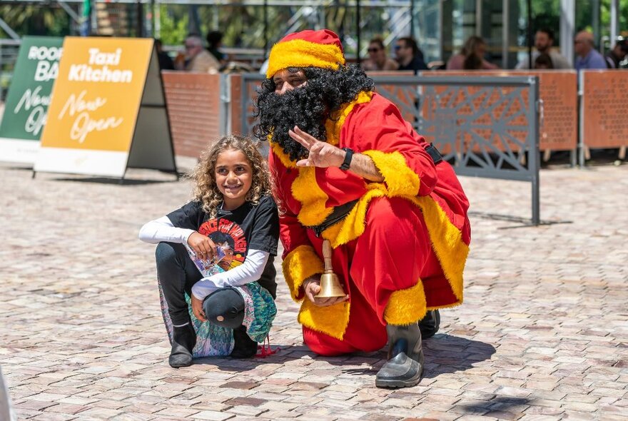 Koorie Klaus squatting on the ground and posing for a photo with a child at Fed Square's main plaza.