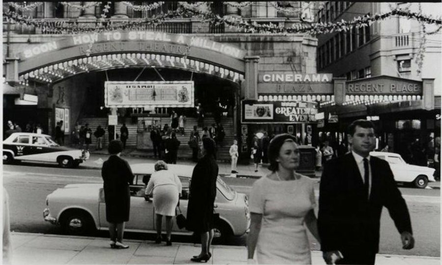 A black and white photo of people milling about outside a theatre