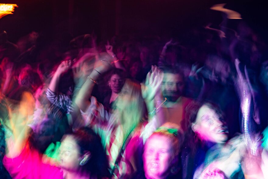 People blurred and in motion, dancing in a darkened club space.
