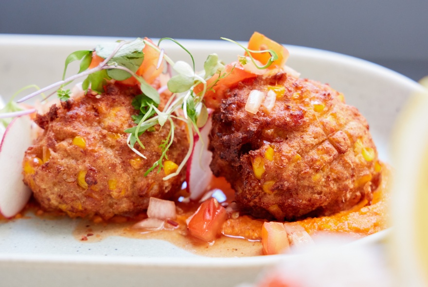 Two arancini balls on a white plate, with a garnish of micro greens and salsa.