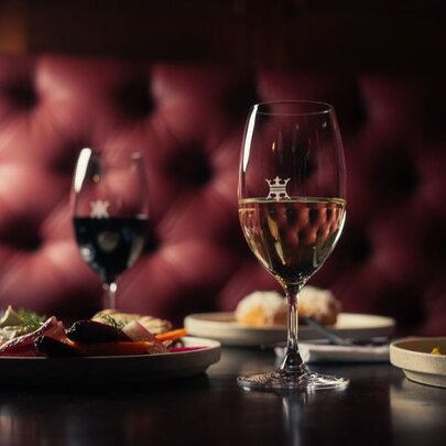 A deep burgundy banquette in a restaurant with glasses of wine and several dishes on the table. 