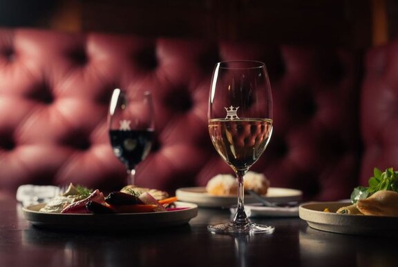 A deep burgundy banquette in a restaurant with glasses of wine and several dishes on the table. 