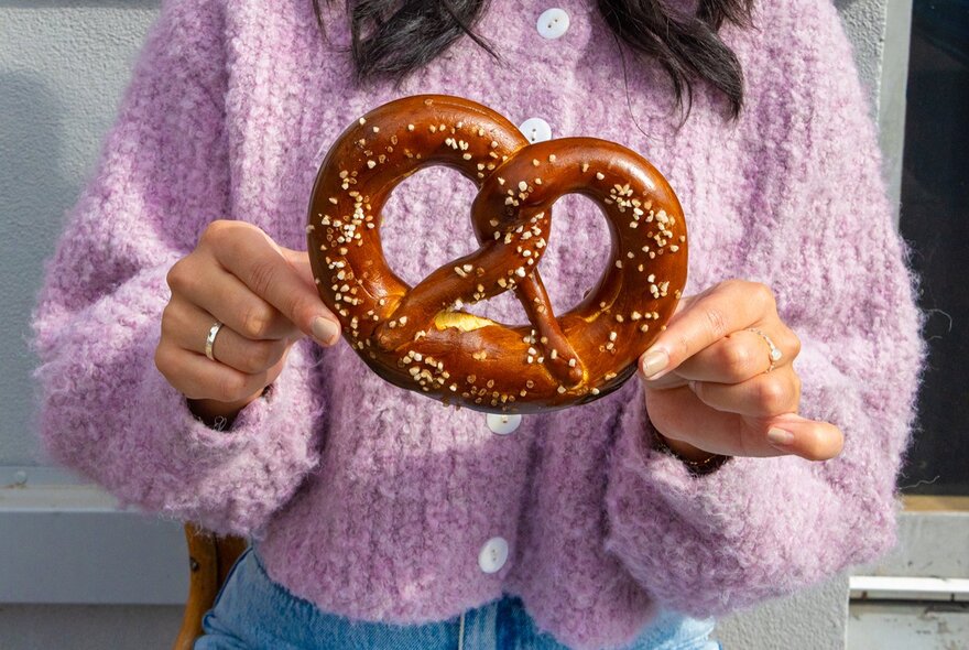A giant German style pretzel held by a woman in a fluffy pink jumper.