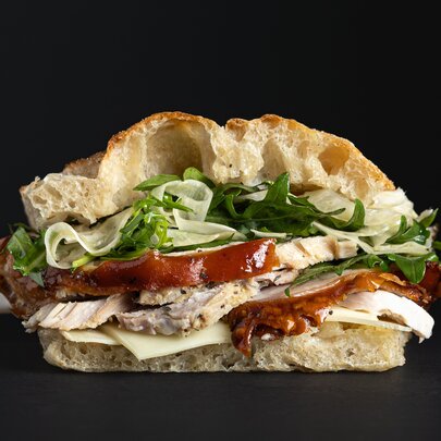 Half a panini sandwich of sliced meat, salad and cheese against a black background.