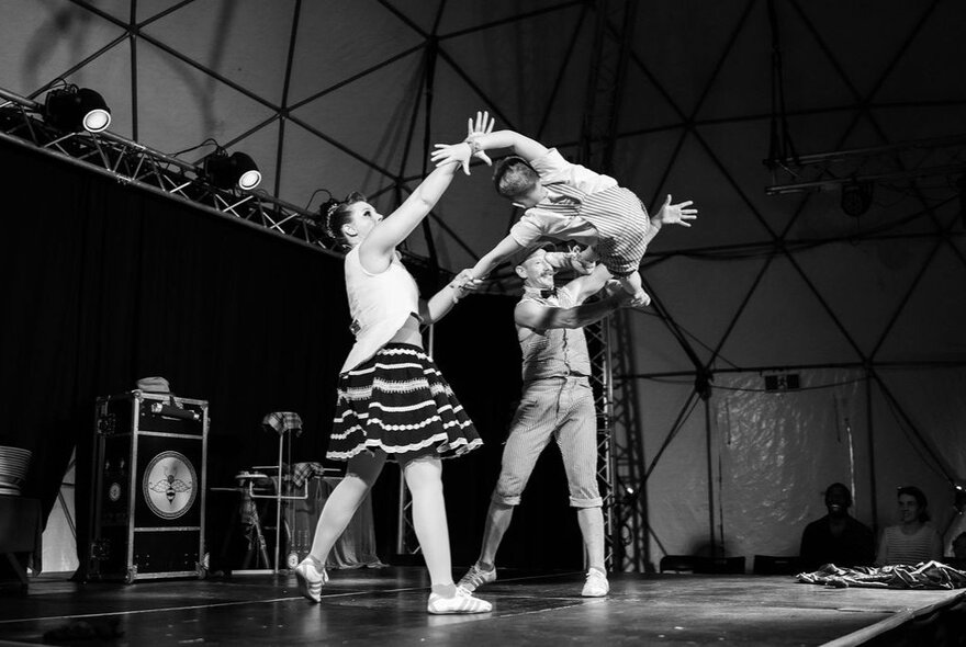 A black and white image of two adult circus performers throwing a child in the air. 