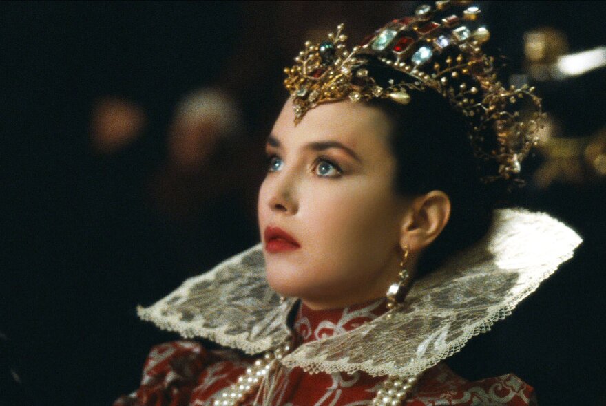 A still from the film La Reine Margot, with an actress dressed as a Queen wearing a crown and an elaborate collared gown.