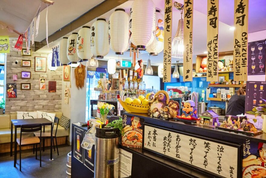 The counter at a homey-looking restaurant, showing many hanging lanterns, small tables, and a bar area.