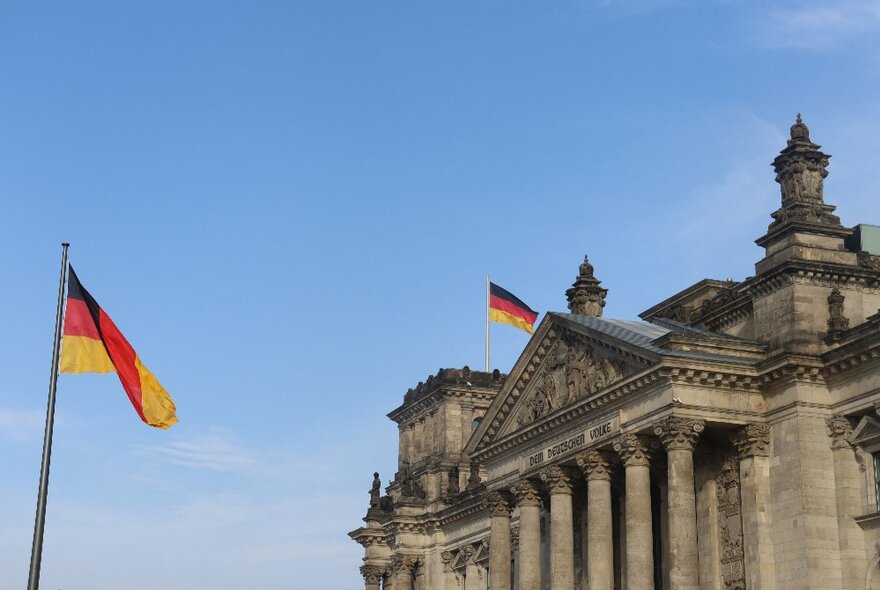 German flags flying outside the Reichstag, a classical building with pedimented portioco.