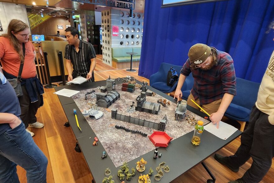 People standing around a table set up for a war game inside a library.
