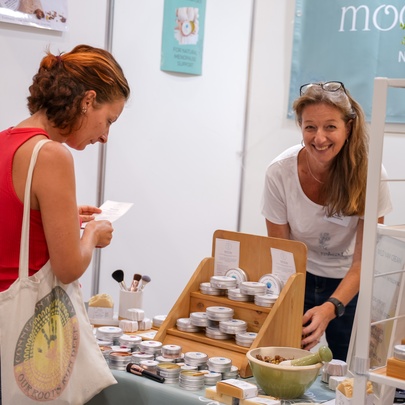 A person browsing a stall at a local market or fair, which feature handmade soaps and natural cosmetics.