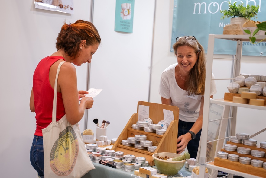 A person browsing a stall at a local market or fair, which feature handmade soaps and natural cosmetics.