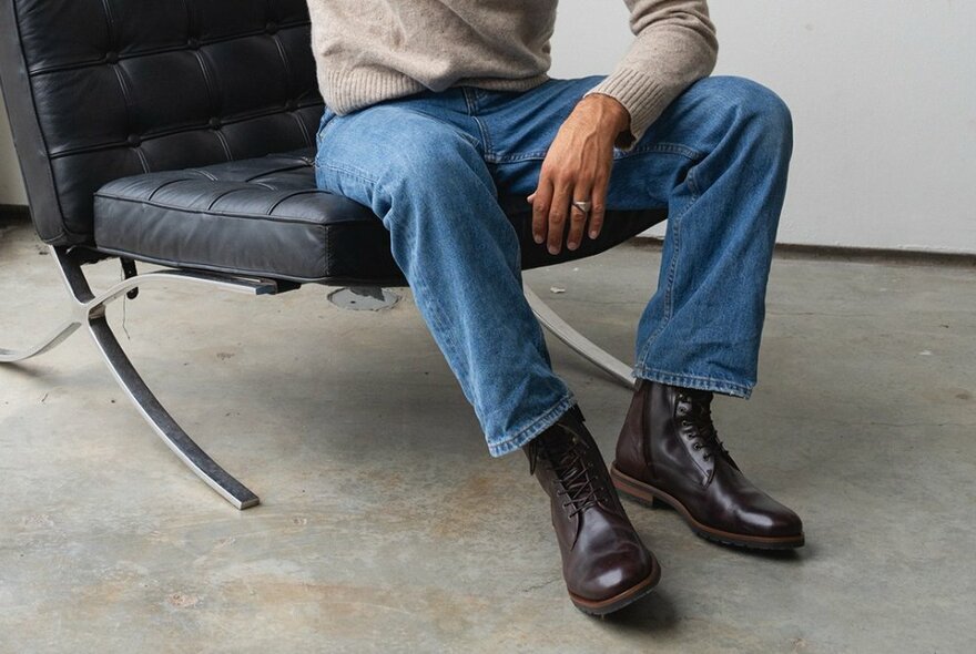 Looking a the bottom half of a man on a leather chair with high leather brown boots on the end of jeans.