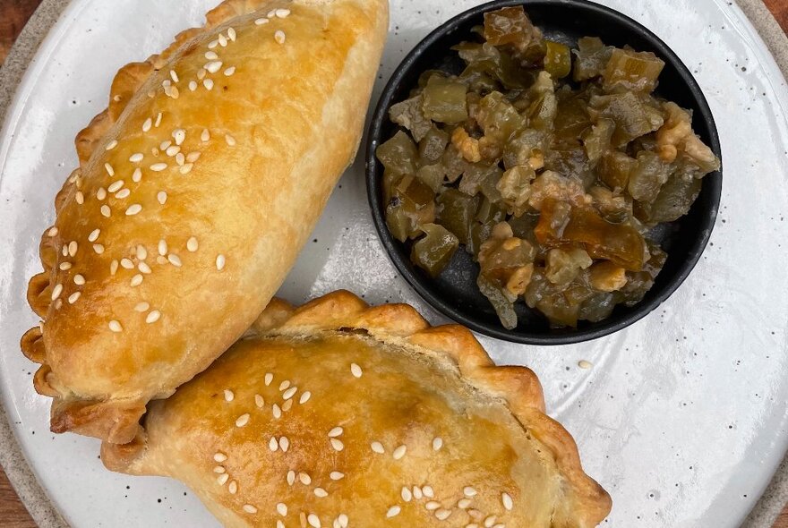 Two cooked and filled pastries or empanadas on a white plate, with a relish on the side.