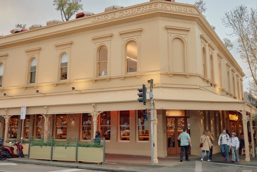 Venue exterior on corner site, older Victorian-era facade with verandah and arched windows, pedestrians passing.