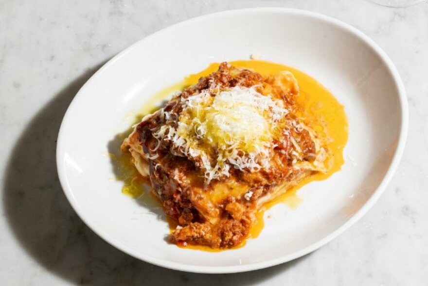 A slice of lasagne with lots of sauce and grated parmesan on top.