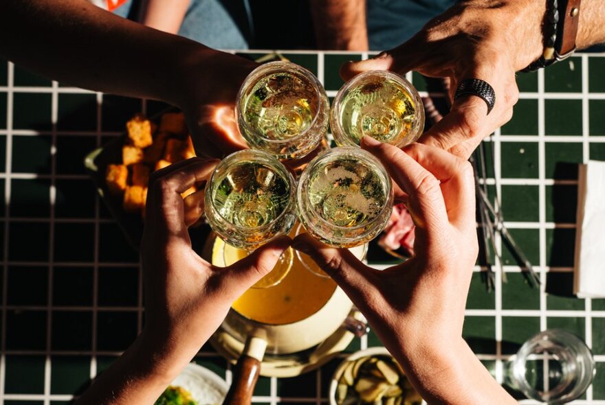 Hands clinking glasses of bubbles over a black-tiled table with nibbles.