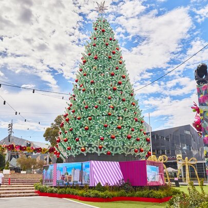 A large, outdoor Christmas tree with red baubles, pink decorations underneath it..