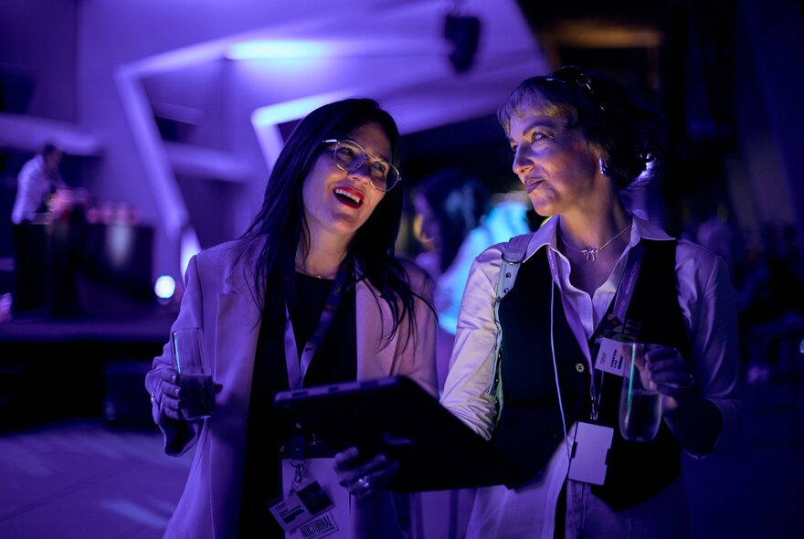 Two individuals talking to each other inside Melbourne Museum at night, with blue lighting.