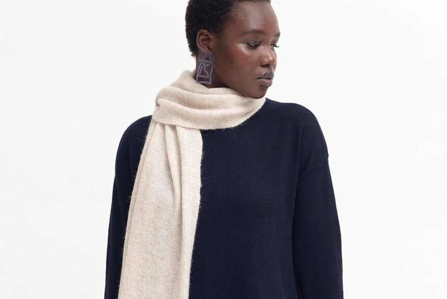 A woman wearing a navy sweater and a cream scarf.