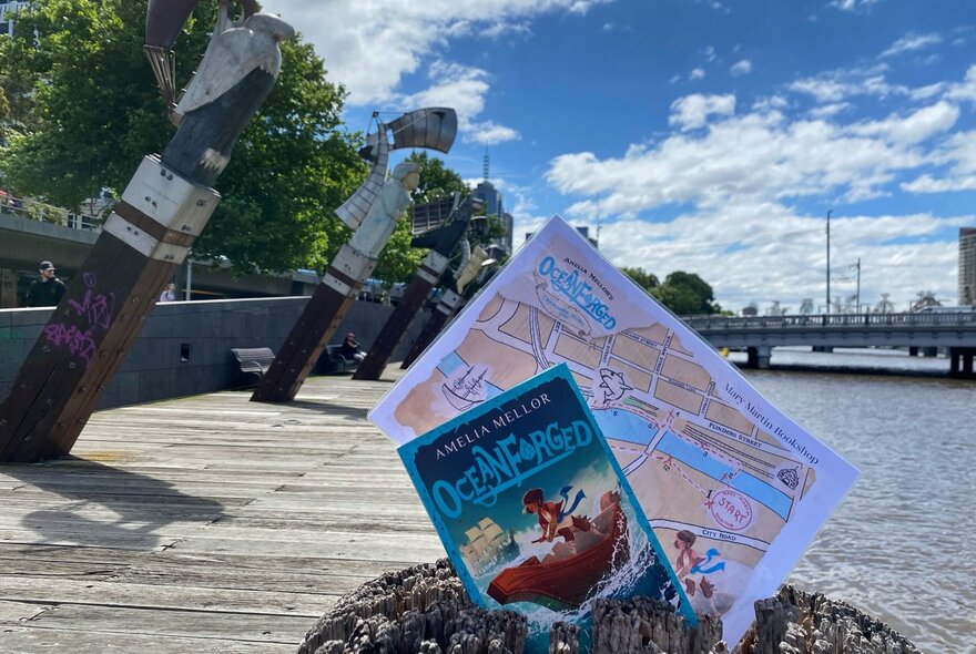 A book and treasure map displayed at a wharf, a river and a bridge in the background.