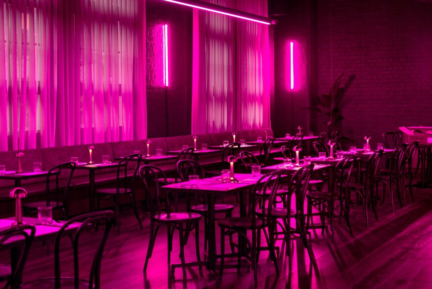 A darkened, empty restaurant space lit up only by a pink neon light.