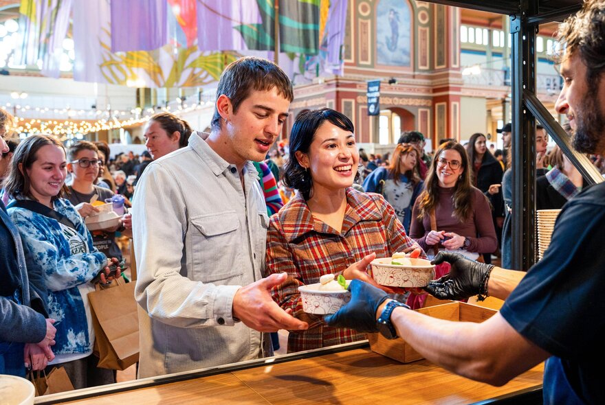 People being handed plates of food at a stall at the Big Design Market inside the Royal Exhibition Building.