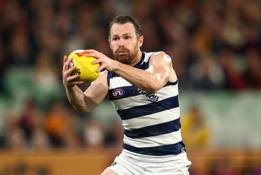 A Geelong AFL player holding a yellow football while moving on the field.