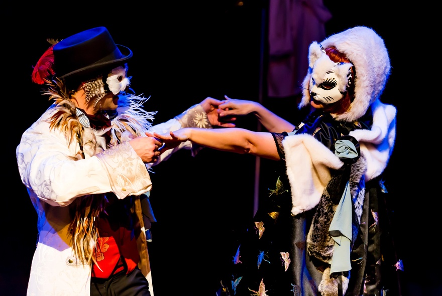 Two performers wearing costumes and masks on a stage.