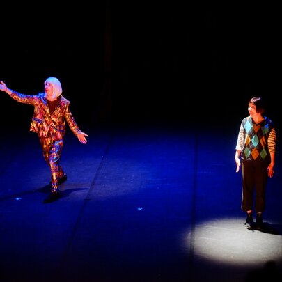 A clown cabaret performance with two people standing on a stage, one of them is spotlit.