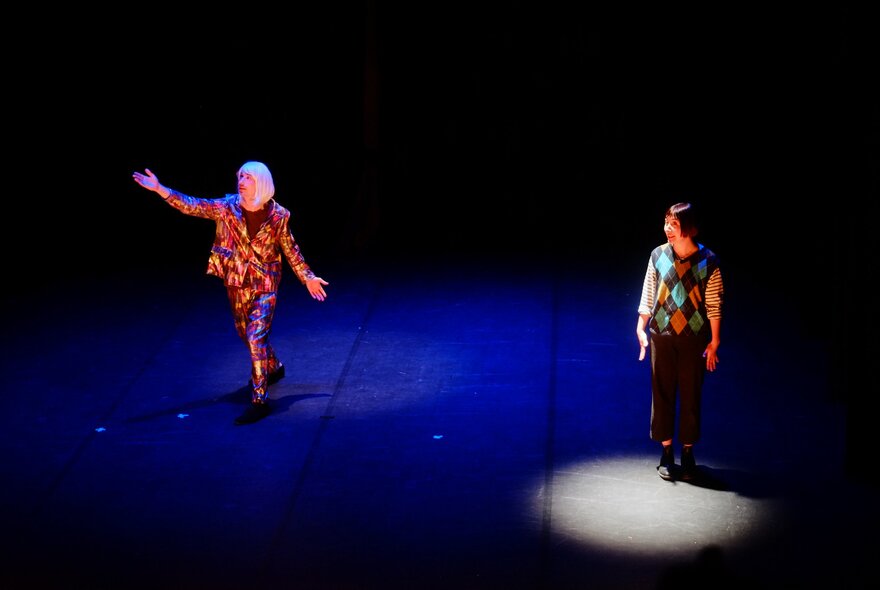 A clown cabaret performance with two people standing on a stage, one of them is spotlit.