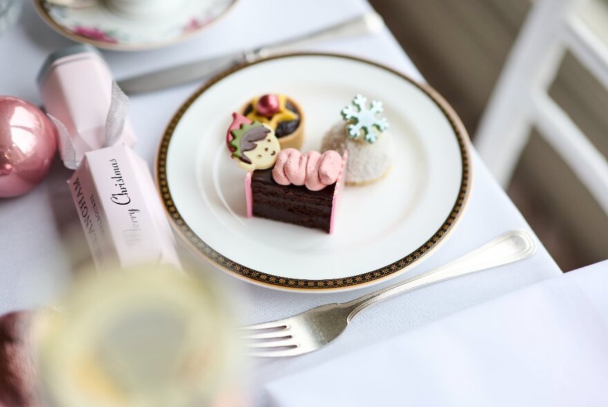 Three festive cakes on a plate with pink crackers and baubles.