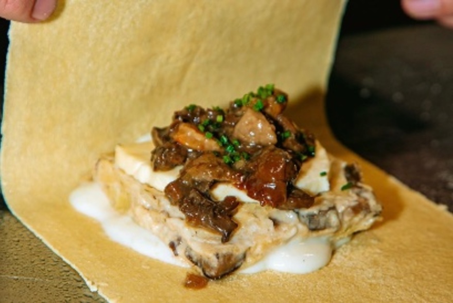 A long lasagne shet being folded over a mean and sauce combination. 