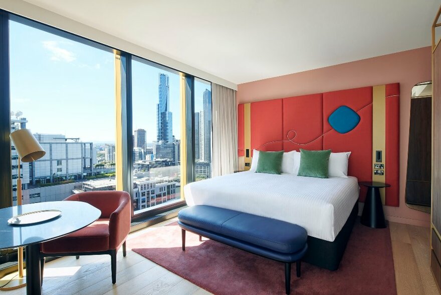 Deluxe suite at the Quincy Hotel Melbourne featuring a king-sized bed, pops of colour and views over the Melbourne skyline.