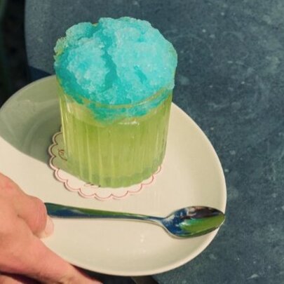 A green cocktail with blue crushed ice on top.