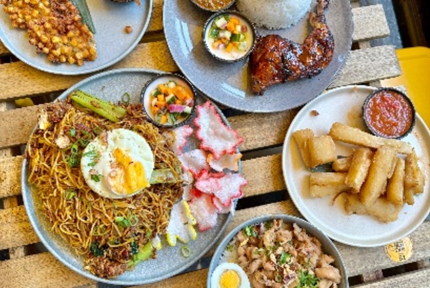 Looking down at a table filled with plates of Indonesian food including a noodle and egg dish, fried chicken and rice, all served with small bowls of sauce.