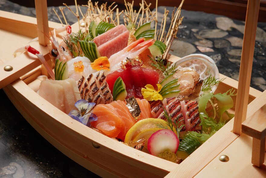 Wooden box of Japanese ingredients including fish and vegetables.