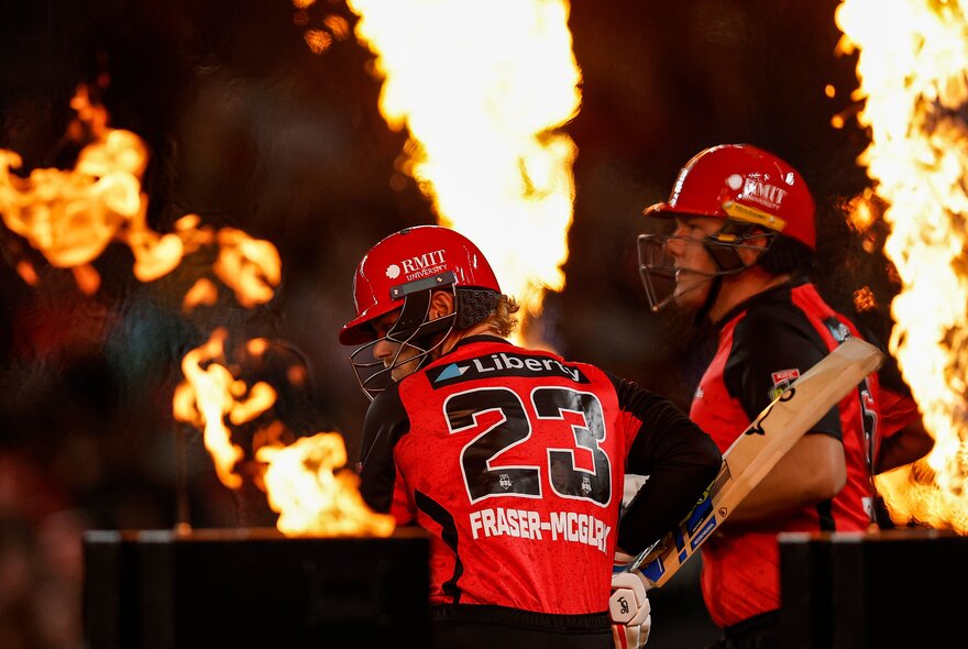 Melbourne Renegades BBL players on the cricket field, one holding a cricket bat, with flames in the background.