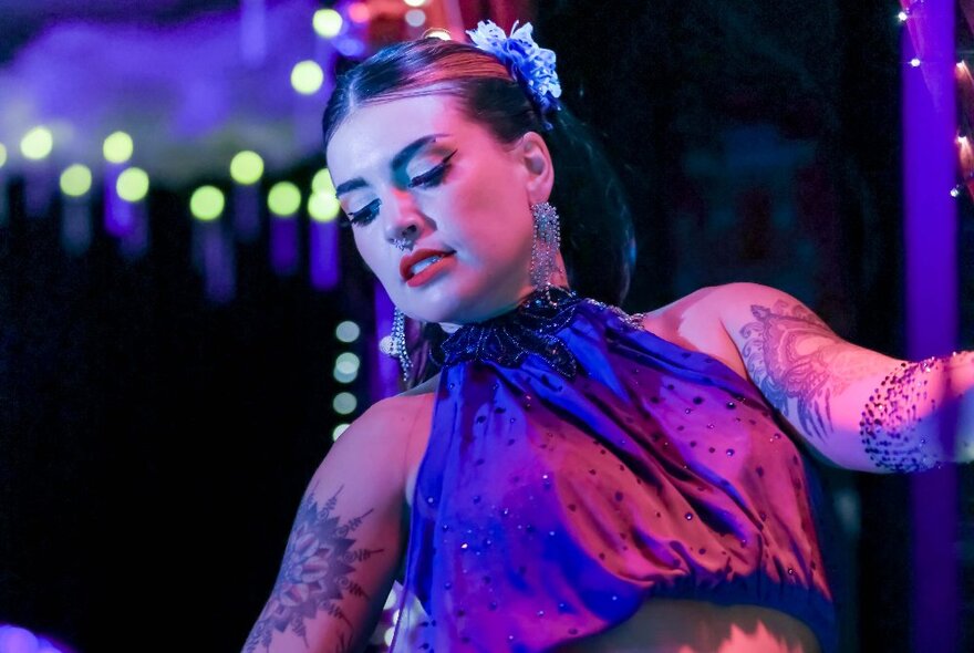 A performer on stage wearing a purple halter top, leaning backwards and looking down.