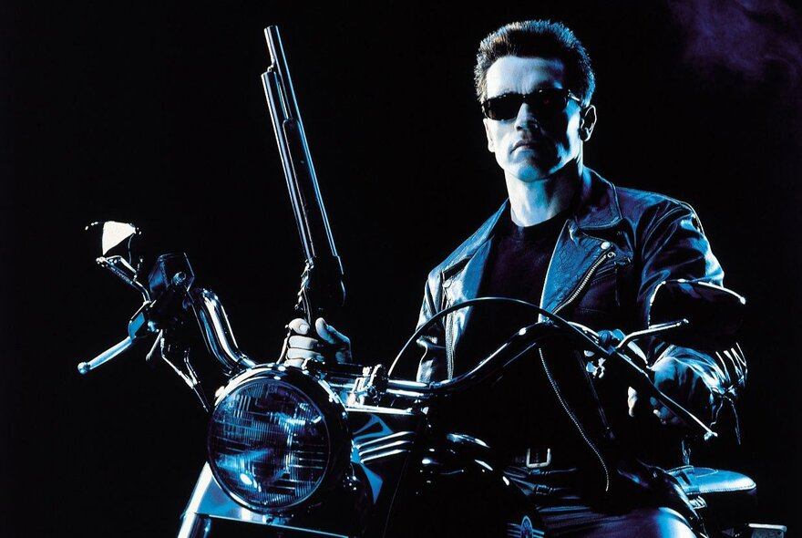 A still from the film, Terminator 2: Judgement Day, showing Arnold Shwarzenegger as the Terminator on a motorbike, holding a shotgun.