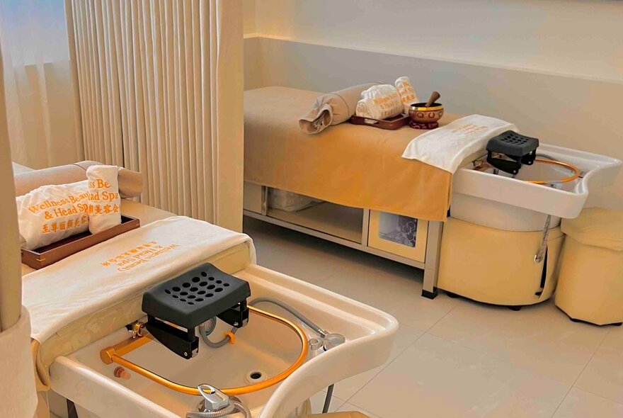 The interior of a specialised spa treatment room, with two treatment beds and a curtain pulled back between them.