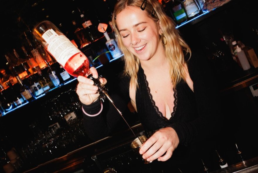A woman pours a shot of a spirit into a jigger from a height.