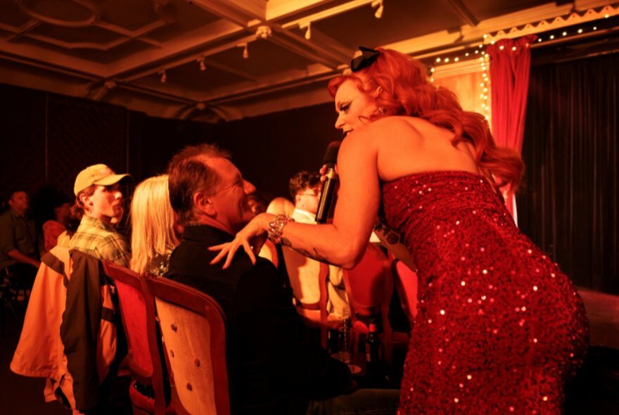 A performer interacting with a seated audience member in a small cabaret venue.