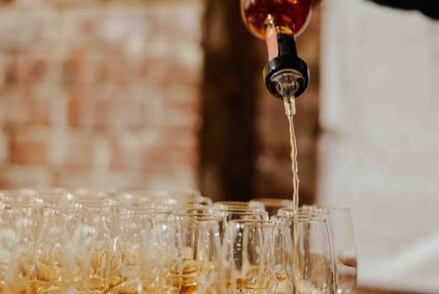 A bottle pouring liquor into a line-up of glasses.