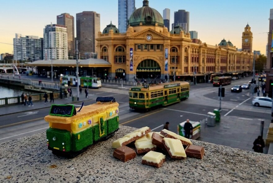 A mini Melbourne tram made out of chocolate, sitting of a concrete ledge next to top deck Belgian chocolate pieces.