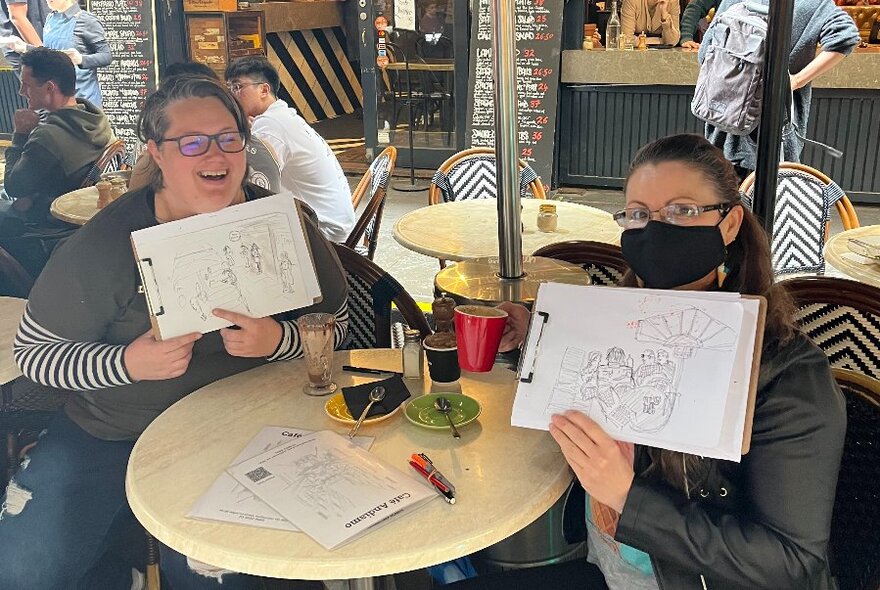 People seated at a cafe holding up examples of their artwork.