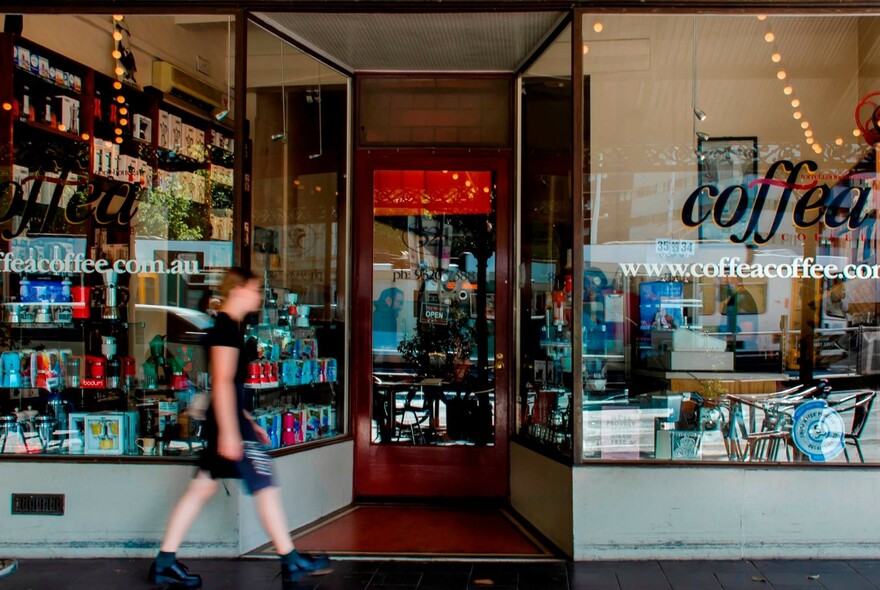 Person walking past Coffea glass shopfront with window displays, tables and chairs.