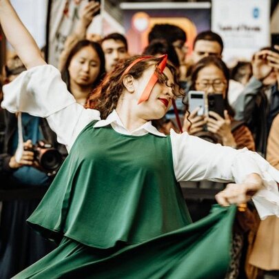 A Persian dancer wearing a traditional green top and skirt, a crowd watching as she dances.