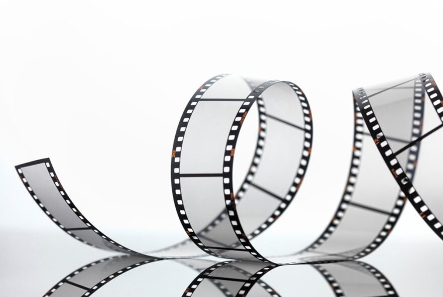 A black and white minimalist shot of a strip of 35mm movie film curled in a loose spiral.
