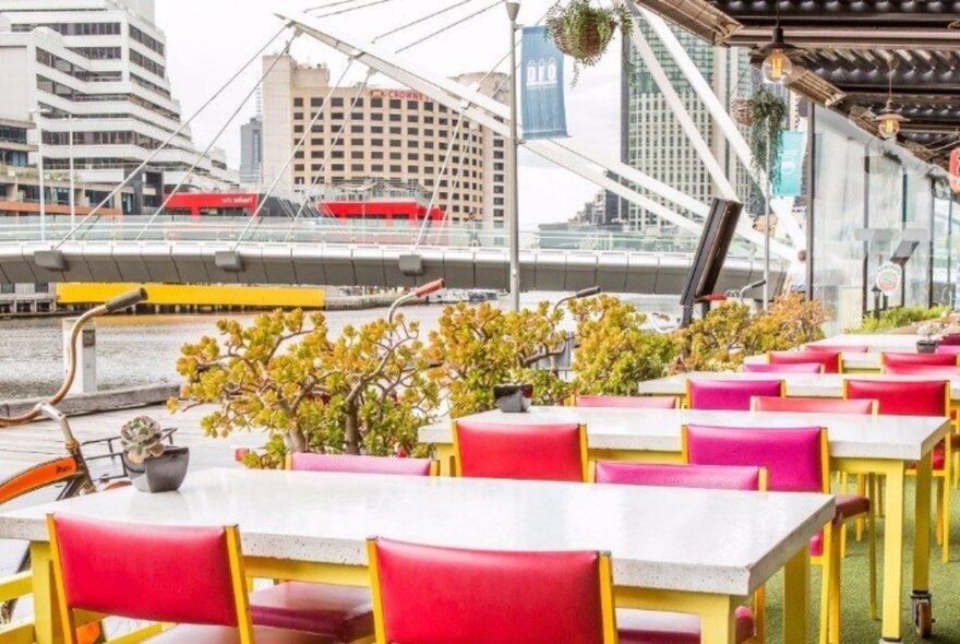 Red outdoor dining chairs and yellow-legged tables by the Yarra River in Melbourne. 