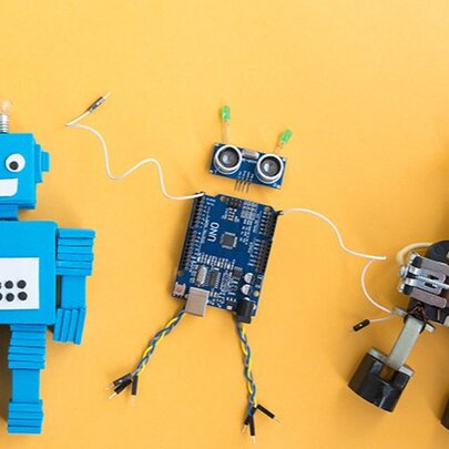 Three toy robots in various stages of being built, on an orange surface.